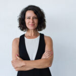 Cheerful middle aged woman with curly hair. Portrait of attractive brunette woman standing with crossed arms and smiling at camera isolated on grey background. Emotion concept